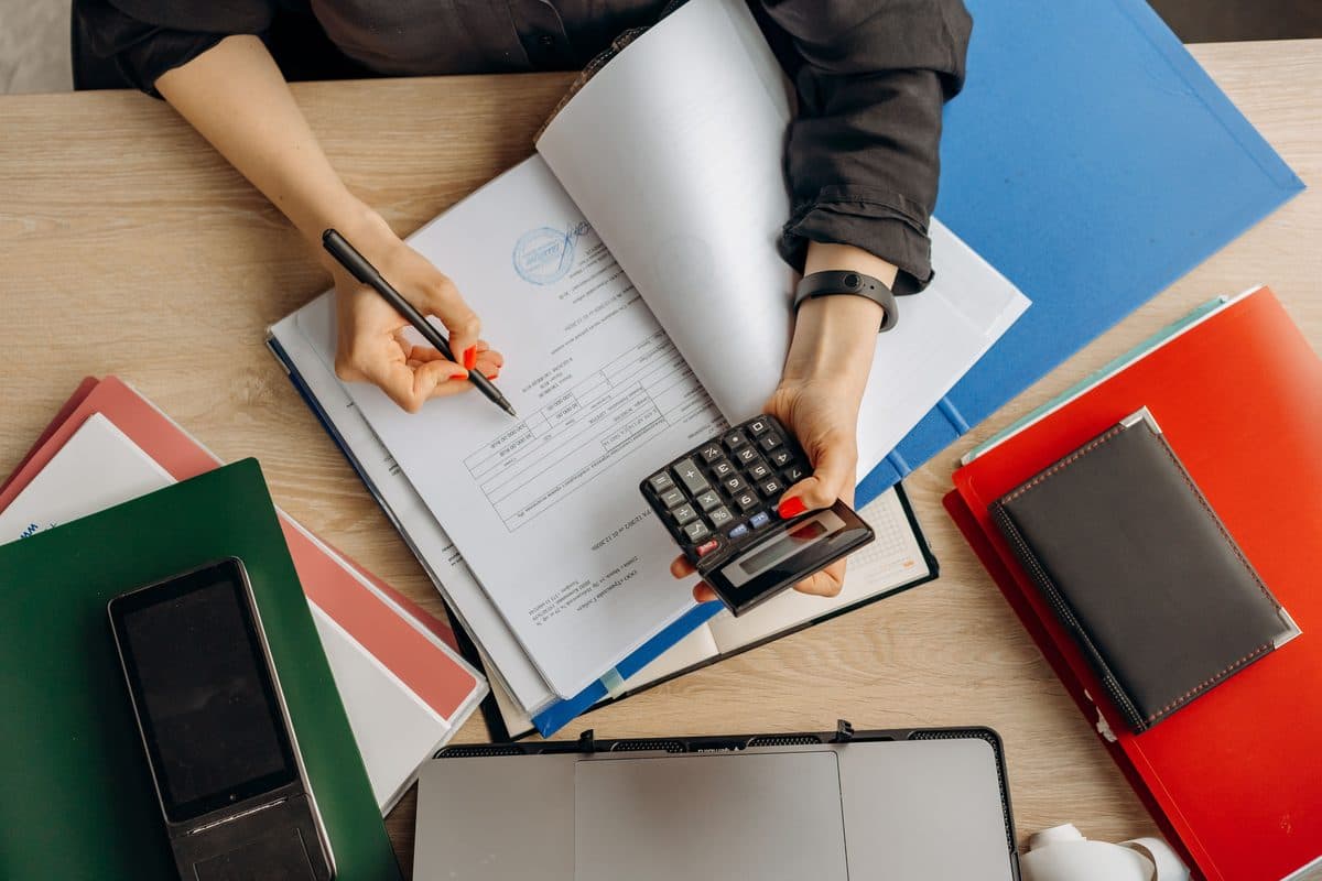 Des mains annotent une déclaration à côté d’une calculatrice et de dossiers.